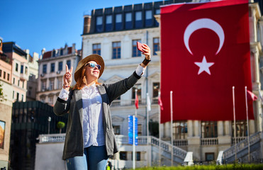 Wall Mural - Attractive young woman tourist takes selfie on background of Turkish flag on Beyoglu Municipality building in Istanbul