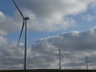 Row of three wind turbines with a cloudy sky in the background