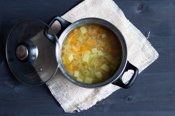 Canvas Print - Pot with open cap with vegetable transparent cabbage soup on fabric cover on black wooden background