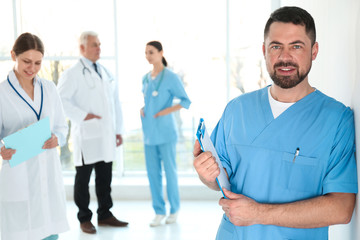 Wall Mural - Mature doctor with clipboard and colleagues in hospital. Medical service