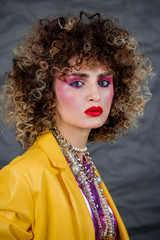 Wall Mural - Portrait of a girl in a yellow jacket and blue jeans with afro hair of the eighties, disco era. Photo in studio on a gray background.