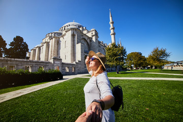 Wall Mural - Follow me. A woman tourist in a hat leads her friend to the Turkish mosque Suleymaniye, Istanbul, Turkey. Travel and religion concept.