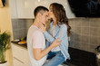 © deineka - Young guy hugs the his girl, the girl kisses the guy on the forehead. Loving young couple in the kitchen having a great time together. Relationship concept.