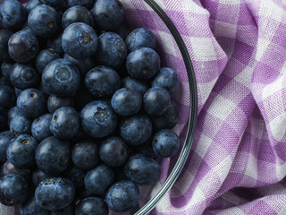 Ripe juicy blueberries in a glass bowl near checkered kitchen napkin. Fruits and berries, vegetarian and healthy eating. Super food. Ready to eat.