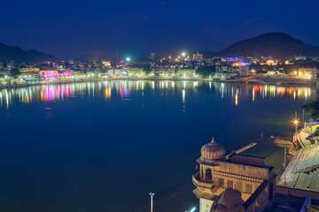 Fototapete - Night view of famous indian hinduism pilgrimage town sacred holy hindu religious city Pushkar with Brahma temple, aarti ceremony, lake and ghats illuminated. Rajasthan, India. Horizontal pan