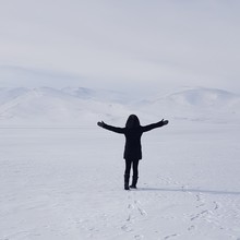 Rear View Of Woman With Arms Outstretched Standing On Snow Covered Field