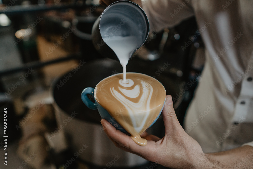 mano de barista haciendo un dibujo de corazón en una taza de café derramando café sobrante, semejante a salvador dalí - obrazy, fototapety, plakaty 
