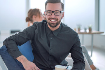 Poster - young businessman with a Cup of coffee sitting in a modern office.