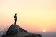 © bilanol - Silhouette of a woman hiker standing alone on big stone at sunset in mountains. Female tourist on high rock in evening nature. Tourism, traveling and healthy lifestyle concept.