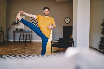 Fototapete - Concentrated man standing on one leg doing yoga exercise in house