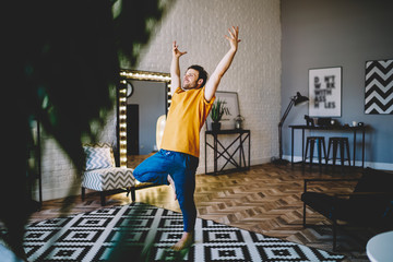 Fototapete - Joyful guy standing on one leg meditating at home