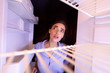 Young woman looking at empty shelves of her refrigerator