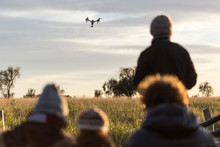 Rear View Of People On Field With Drone Flying Against Cloudy Sky