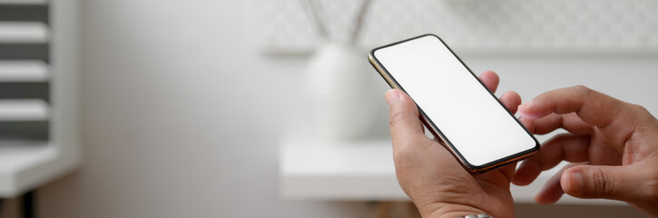 Wall Mural - cropped shot of male freelancer using mock-up smartphone at minimal home office