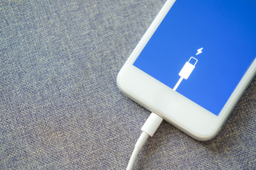 Smartphone fast charging using USB cable. Selective focus with blurry fabric background.