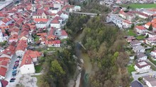 Forward High Flying Drone Aerial View Of Old Downtown Of Kranj Town, Slovenia Over Canyon With A Damn On River