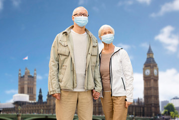 Wall Mural - health, quarantine and pandemic concept - senior couple wearing protective medical mask for protection from virus holding hands over london city, england background