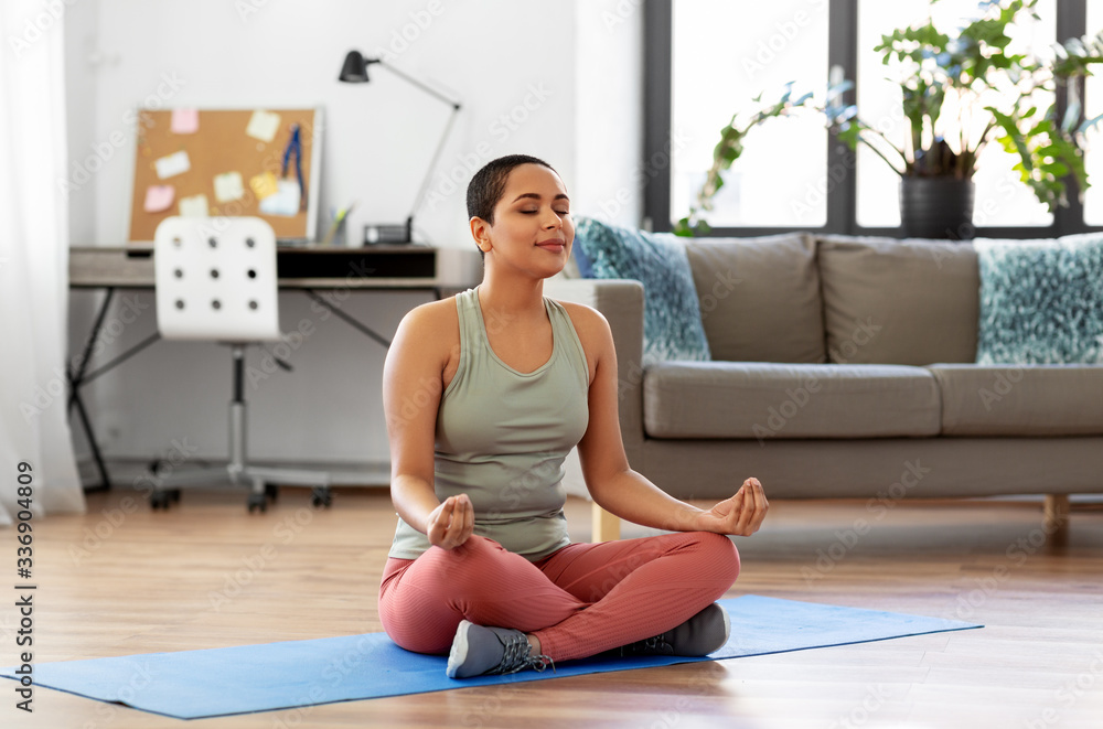 yoga, mindfulness and healthy lifestyle concept - happy young african american woman meditating in lotus pose at home - obrazy, fototapety, plakaty 