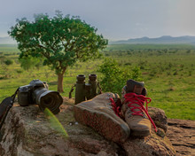 Pair Of Boots, Binoculars And Photography Camera Displayed In A Rock After A Hiking Activity In The Mountains, Uganda, Africa