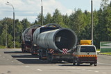 Fototapeta  - Long oversized cargo transportation logistics, large long tubes on low-frame trawls trucks with an escort car on asphalt road