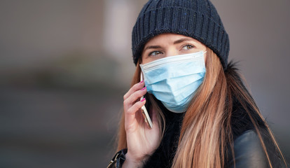 Wall Mural - Young woman wearing disposable blue virus face mouth nose mask talking on mobile phone. Closeup detail, can be used during coronavirus covid-19 outbreak prevention