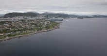 Approaching Aerial Hyperlapse Of A Luxurious Cruise Ship That Is Leaving The Port Of Alesund, The Most Beautiful Town Of Norway, While A Tugboat Performs A Water Salute By Spraying Water In The Air.