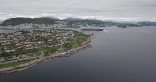 Approaching Aerial Drone Footage Of A Luxurious Cruise Ship Leaving The Bay Of Alesund, The Most Beautiful Town Of Norway, While A Tugboat Performs A Water Salute By Spraying Water In The Air.