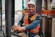 © StratfordProductions - Portrait of happy driver wearing white helmet and vest sitting in forklift machine transporting goods in warehouse