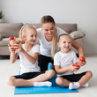 © FreepikCompany - Front view of mother posing with daughters at home while holding weights