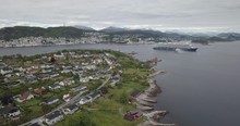 Approaching Aerial Footage Of A Luxurious Cruise Ship That Is Leaving The Bay Of Alesund, The Most Beautiful Town Of Norway, While A Tugboat Performs A Water Salute By Spraying Water In The Air.