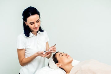 Wall Mural - Cosmetologist and patient while eyelash extension procedure on white background with copy space.