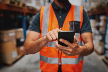 Closeup of man hands using mobile phone while in warehouse in uniform