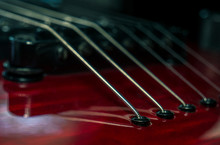 Close Up With A Guitar Bridge And Strings. Red Guitar With Blurred Background.