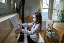 Young Girl Wearing Glasses And Turning The Page Of Her  Music Book While Practicing The Piano At Home