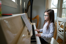 Young Girl Wearing Glasses While Reading Music And Practicing The Piano At Home