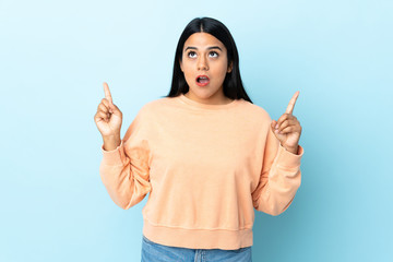 Wall Mural - Young latin woman woman isolated on blue background surprised and pointing up