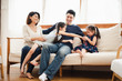 Young Asian warm love family stay in white  living room at home, parent and two daughter enjoy to playing with funny which sitting on white sofa, looking smiling and felling happy.