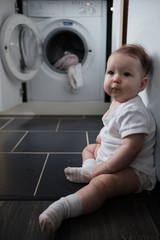 little blue-eyed girl sitting near the washing machine. Baby and laundry. household chores and children