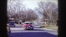 IDAHO-1955: Older Vehicles Parked And A Red Vehicle With White Stripe Driving Down Street