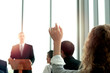 © Stella - Young woman raising hand up to ask question with speaker in the meeting room seminar conference
