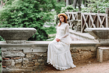 girl in a white dress and a straw hat walks in a beautiful park. bride in a vintage wedding dress in the garden.