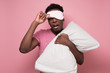 © Viktor Koldunov - Handsome sleepy african american man in blanket and mask looking on what is happening around. Studio shot on pink wall