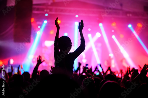 a silhouette of an applauding crowd in front of a stage in pink light. banner for a music festival. poster of the upcoming show.