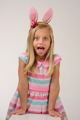 beautiful girl with pink bunny ears shows her tongue supported on a white box on a gray background