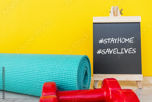 Blackboard with words #stay home #save lives and yoga mat and pink dumbbell -  Corona virus Covid - 19 lock down, restricted movement and workout exercise concept.