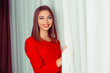 © hbrh - Portrait of a young smiling woman  in red dress opening curtains. Indoors shot, horizontal image