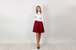 © hbrh - Successful and bold. Full length of happy young businesswoman with crossed arms, standing isolated against white wall. One single person. White shirt, red skirt. Copy space.