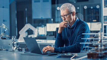 Fototapete - Professional Electronics Design Engineer Wearing Glasses Works on Computer in Research Facility. In the Background Motherboards, Circuit Boards and Computer Components in the High Tech Facility.