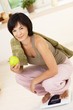 © nyul - Portrait of young woman in sporty clothes, crouching on weight scale, holding green apple, looking at camera, smiling.