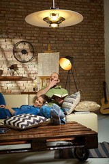 Wall Mural - Couple resting on sofa at home, woman sleeping, man reading and yawning.